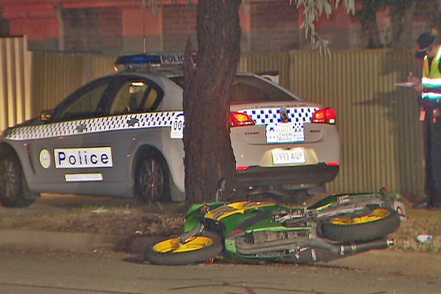 Police car and officer at the scene of an accident with a motorcycle lying on the ground.