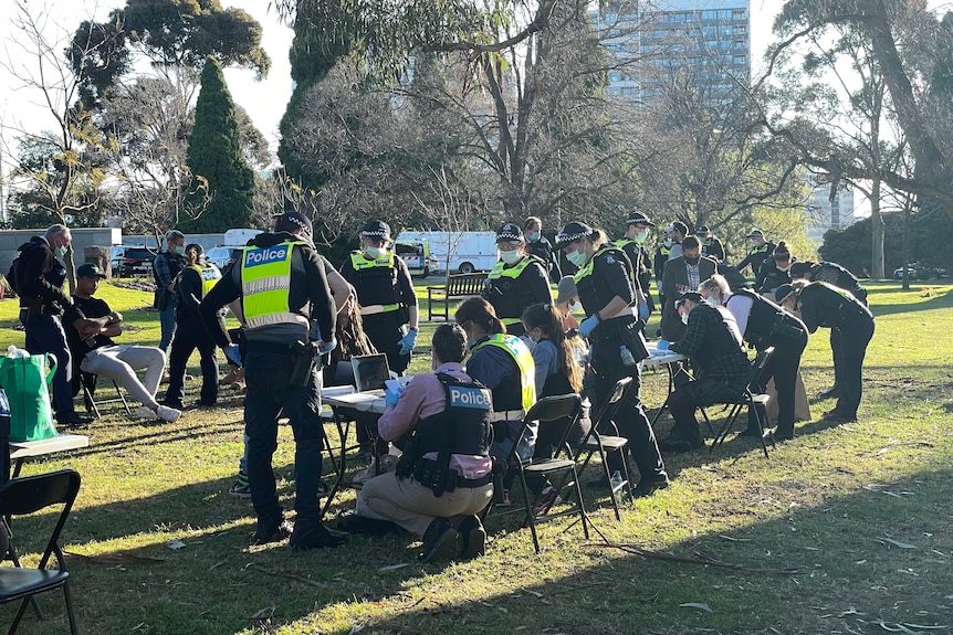 Number of police sit bent over a long desk in a park.