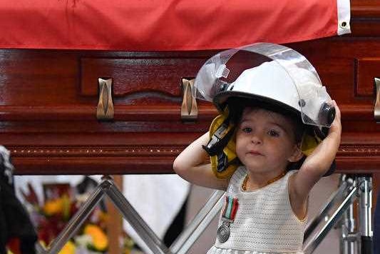 A young girl wearing a helmet in front of a funeral casket.