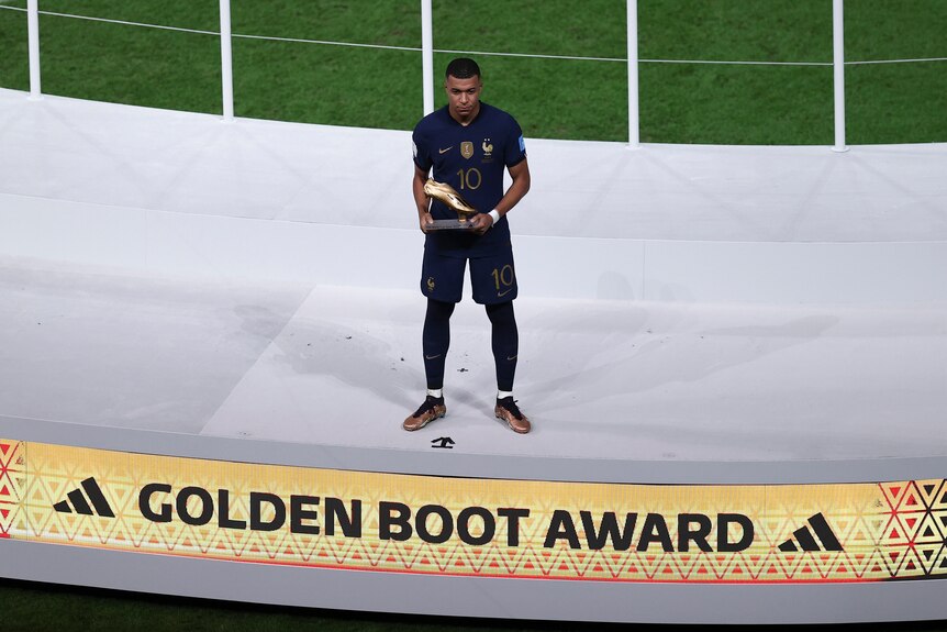 France's Kylian Mbappe stands on a stage with the golden boot award after the 2022 FIFA World Cup final.