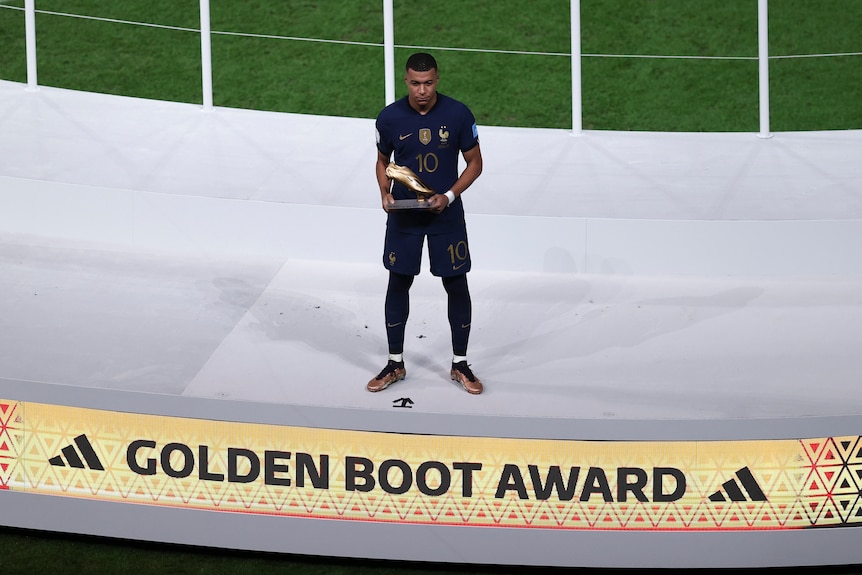 Le Français Kylian Mbappe se tient sur une scène avec le prix du soulier d'or après la finale de la Coupe du monde de football 2022.