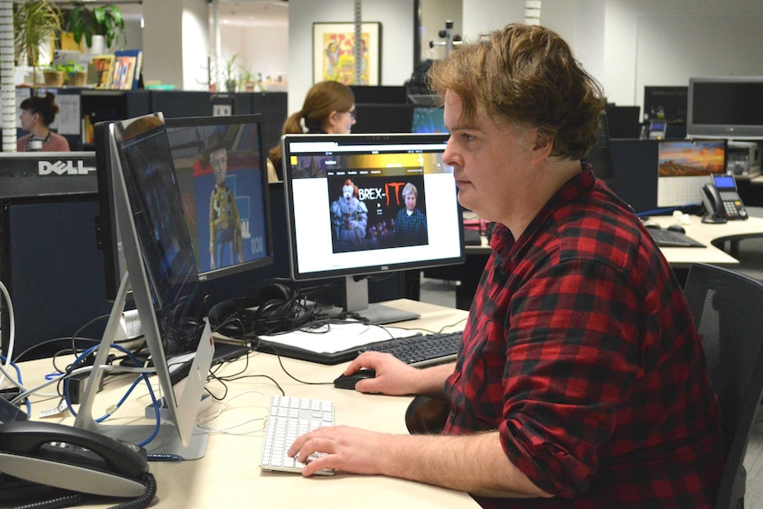 Parkinson sitting at desk in front of three monitors in office.