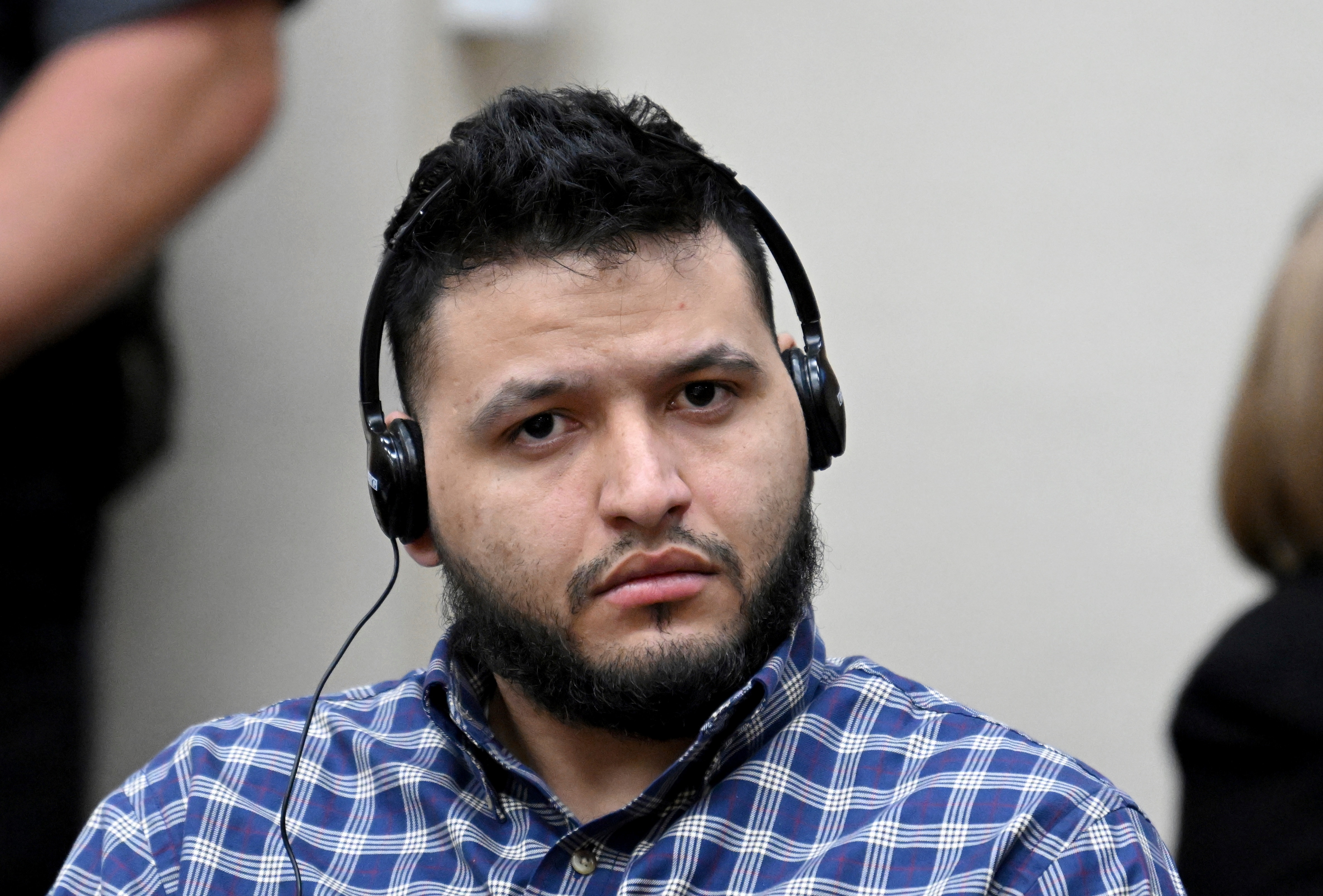 Wearing a checkered button-up shirt, Ibarra listens to an interpreter through headphones