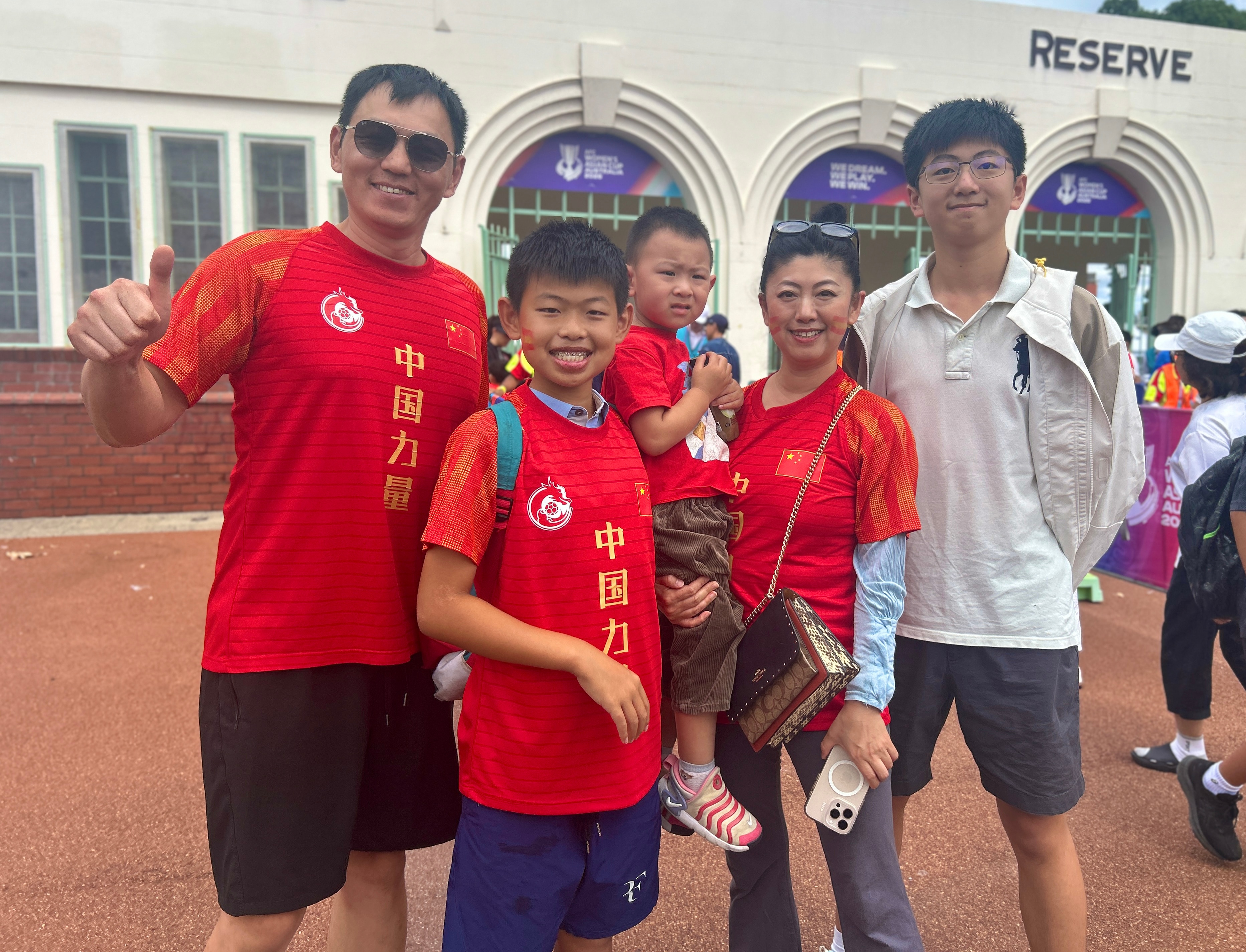 Um grupo de pessoas com camisetas vermelhas da China sorri para a câmera e uma delas é cinza