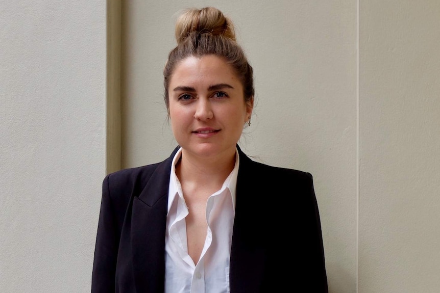 Freelance producer and stylist Ellie Hinkley wearing white shirt and black blazer, standing against a plain wall.