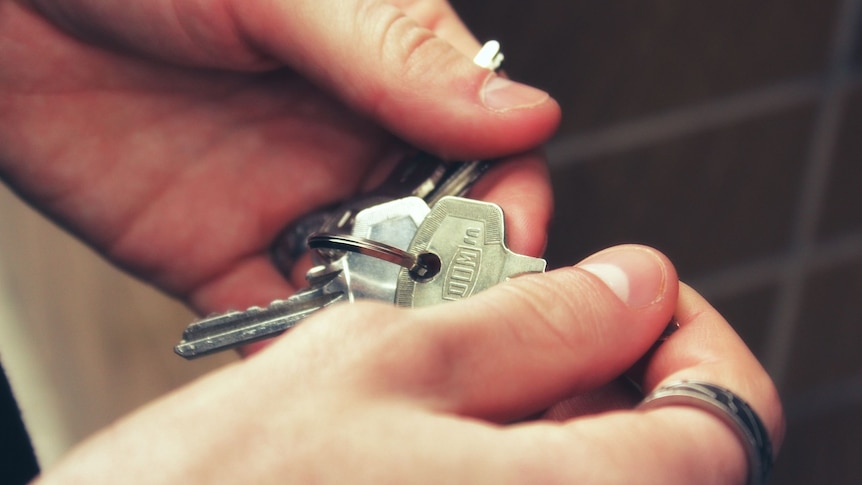 A close-up shot of a person's hands holding a set of silver house keys.
