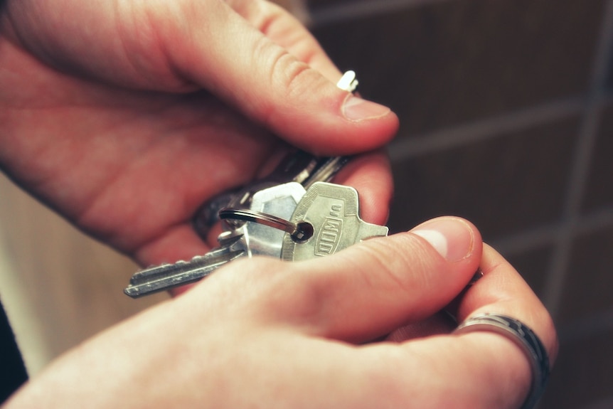 A close-up shot of a person's hands holding a set of silver house keys.