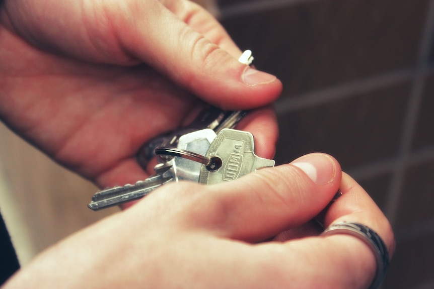 Un gros plan des mains d'une personne tenant un ensemble de clés de maison en argent.