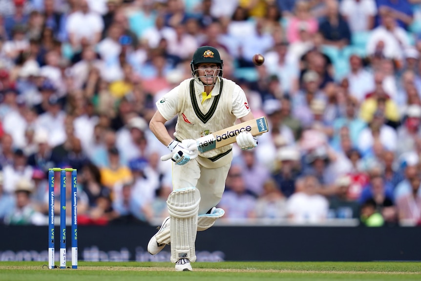 Australia batter Steve Smith takes off for a run as the cricket ball sits in the air in front of him.
