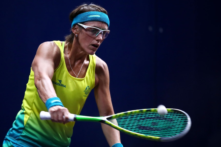 A female squash player wears protective sports glasses and hits the ball with the racquet.