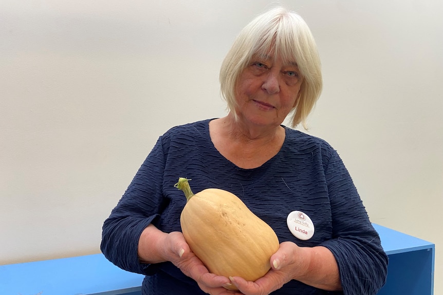 a photo of an older woman with grey hair, holding a pumpkin