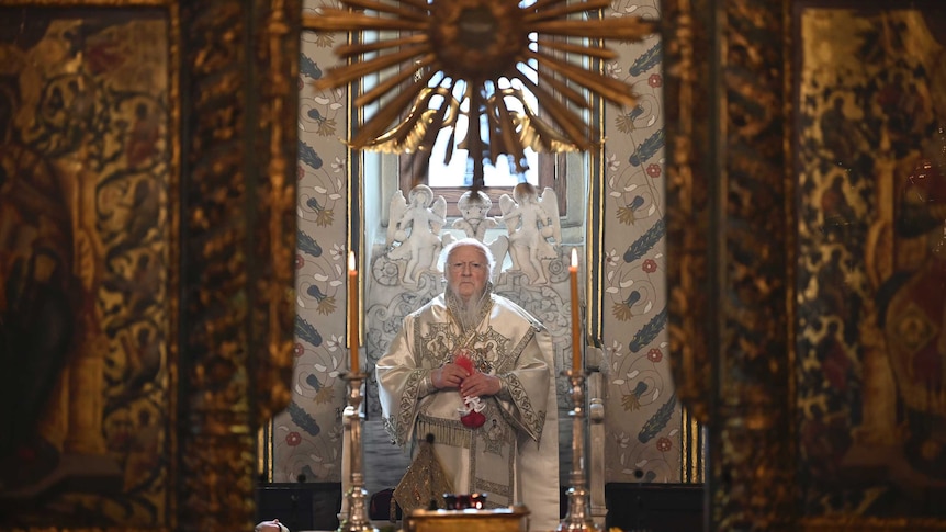 An Orthodox priest looks on in contemplation while sitting on a throne.