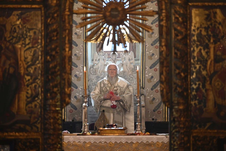 An Orthodox priest looks on in contemplation while sitting on a throne.