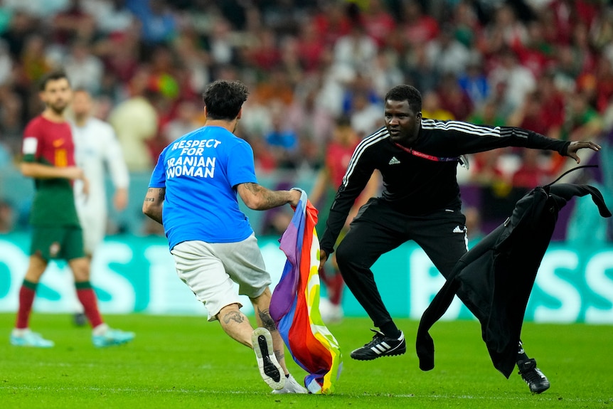 A man in a blue shirt holding a rainbow flag on a soccer field