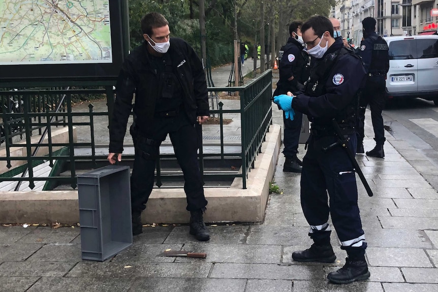 Two police officers in black uniforms stand nearby a meat cleaver on the ground in Paris.