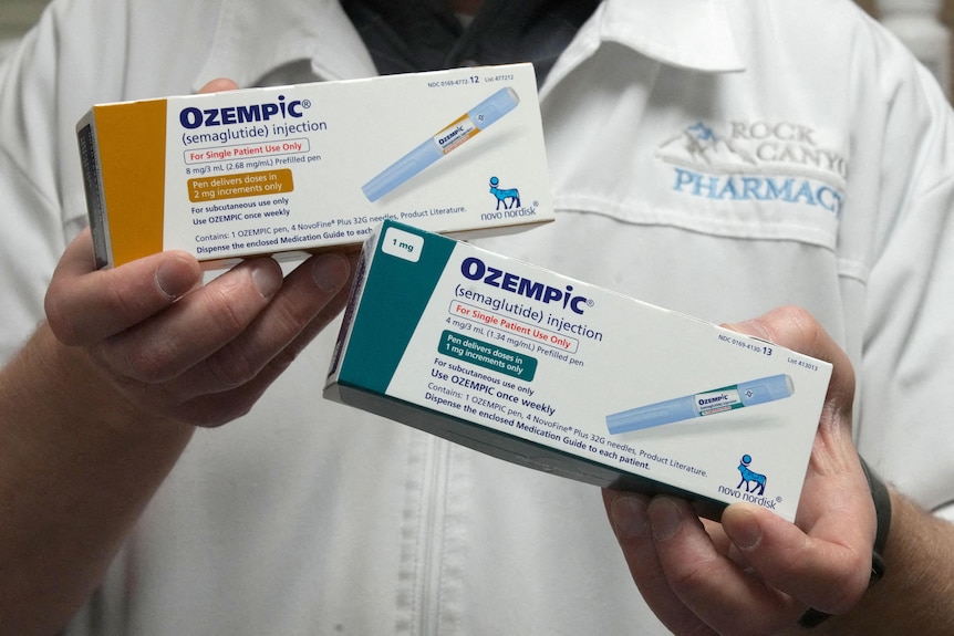 A pharmacist holds up boxes of Ozempic medication. 