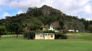 Small sports club rooms can be seen in the middle of an oval, with picturesque land formation Hanging Rock in the background.