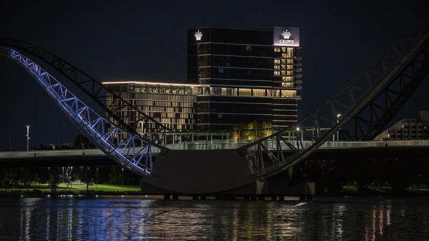 Tall buildings in the dark with lights on and a bridge frame in the foreground illuminated with blue light. 