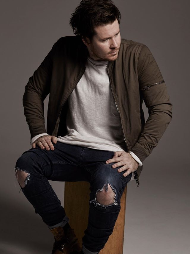 Man with torn jeans sits on stool looking away