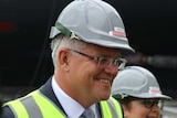 Scott Morrison wearing a hard hat, high-vis vest and smiling with two women in the background