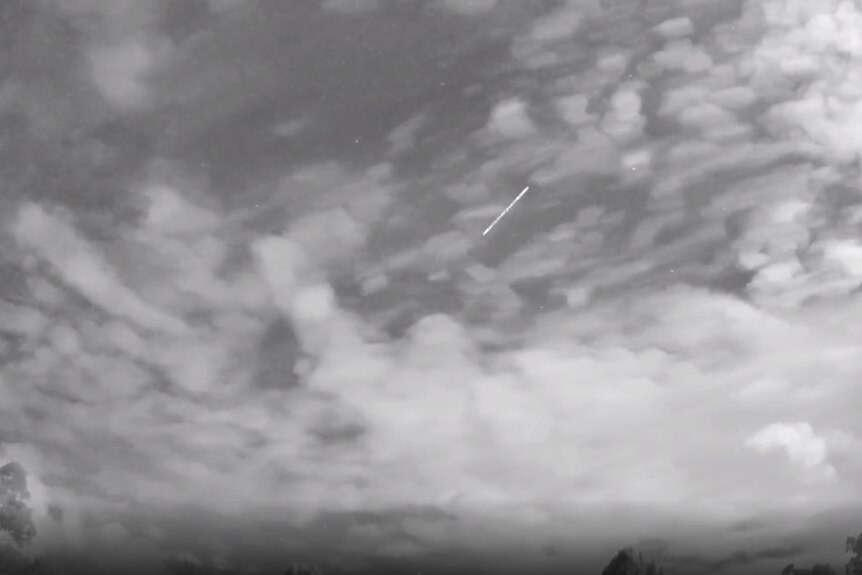 A meteor streaking through a cloudy sky.