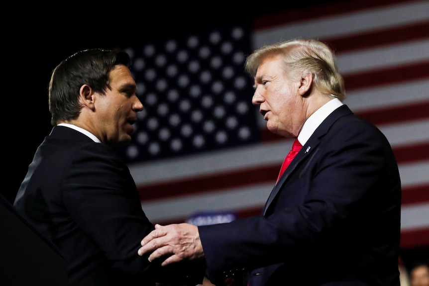 Donald Trump (right) talks with Ron DeSantis on stage.
