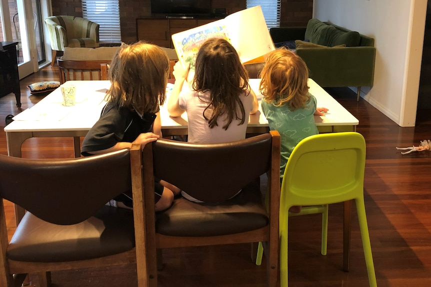 Three girls sitting on chair with back to camera.