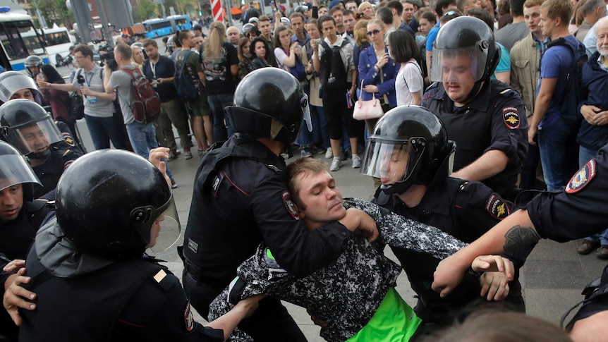 Four police drag protester during rally