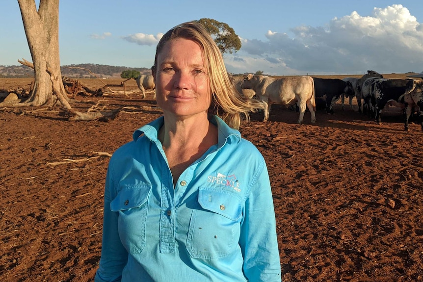 Anne Knoblanche stands in brown dirt with cows behind her.