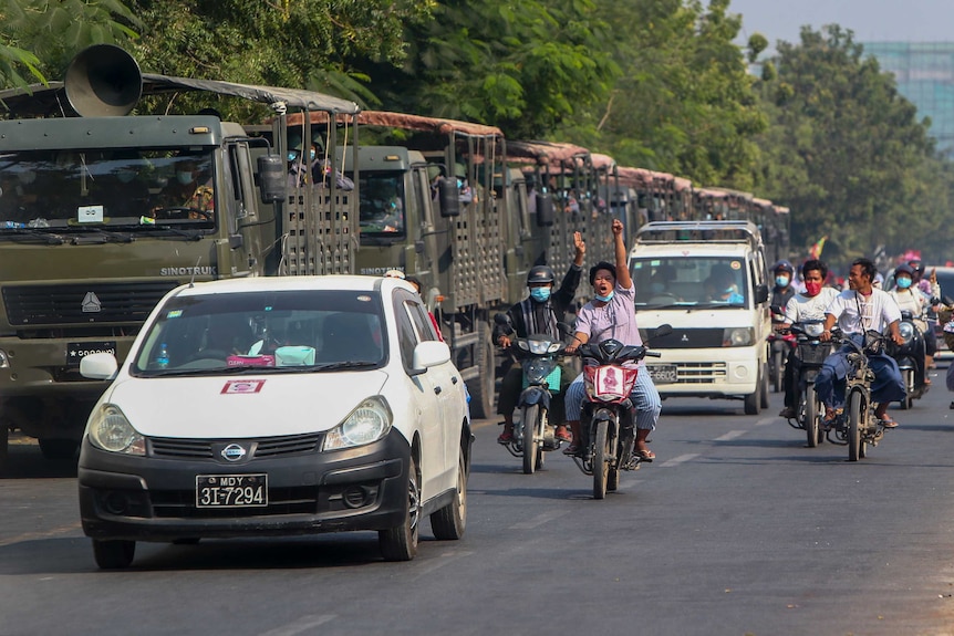 Demonstrators on motor bikes flash the three-fingered salute against the military coup as they ride pass military vehicles