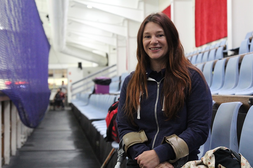Susan Seipel sitting on the front row of a grandstand inside a white-walled ice skating rink.