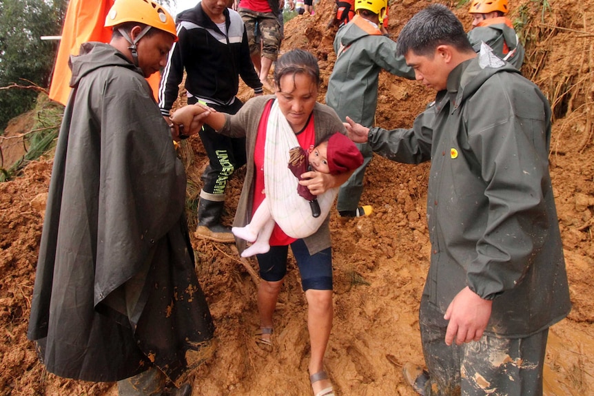Two male rescuers guide a mother and her child over muddy ground as they evacuate from an area hit by landslides.