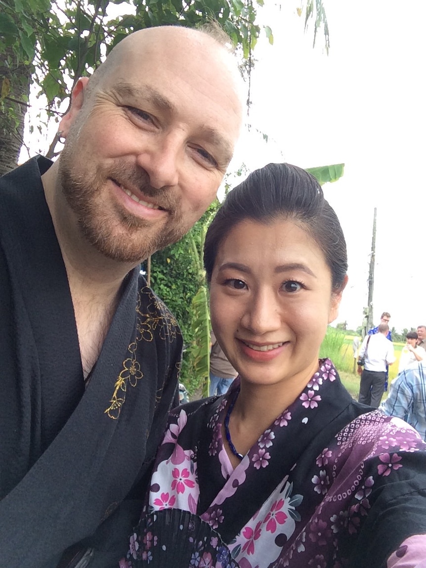 Dominic and Kumi, who are wearing traditional dress, smile for a selfie.