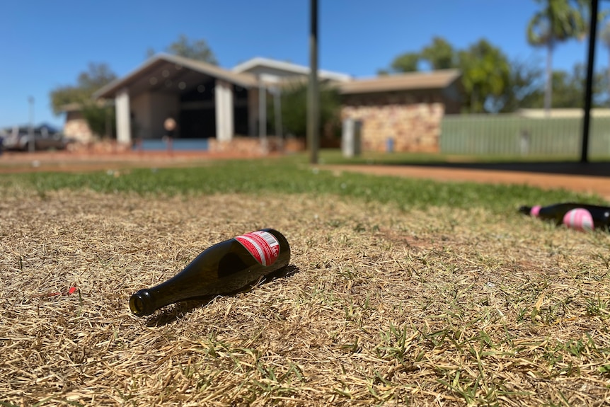 Passionpop bottles on grass, a brick building with sloping roofs in the background, blue sky.