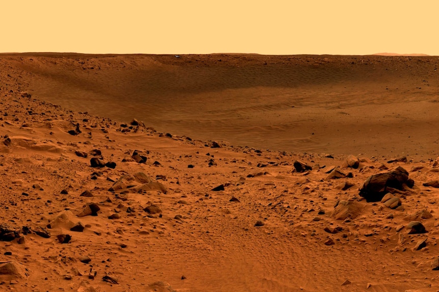 Red dirt and rock dominate this landscape of Mars, and the sky is a light orange