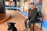 Man sitting outside a doctors surgery with a dog on the lead not smiling.