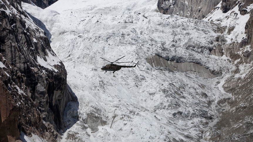 A helicopter flies over a snow covered glacier. 
