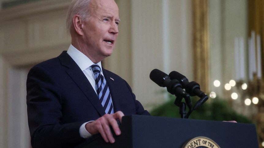 Joe Biden speaks into a microphone at a lectern with a US presidential seal on the front