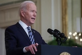 Joe Biden speaks into a microphone at a lectern with a US presidential seal on the front
