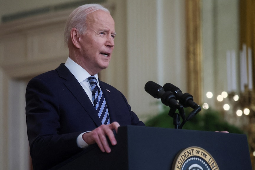 Joe Biden speaks into a microphone at a lectern with a US presidential seal on the front