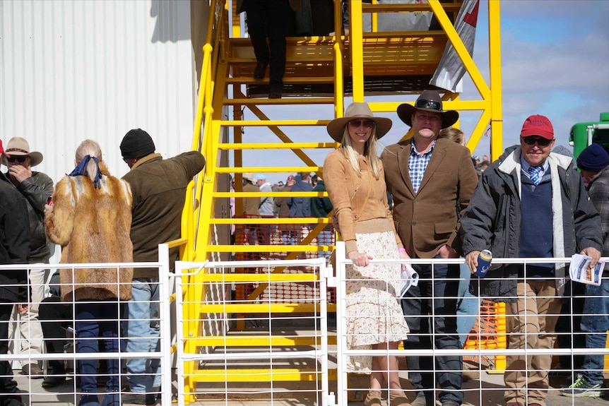 Men and women stand behind a fence trackside and smile at the camera.