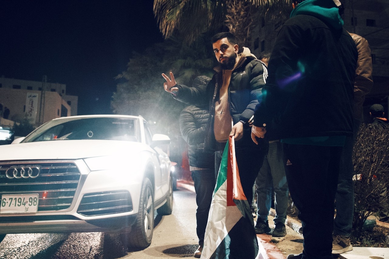 A man standing by the side of a road, giving the peace sign
