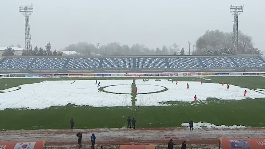 Two soccer teams play in an outdoor field half-covered with snow