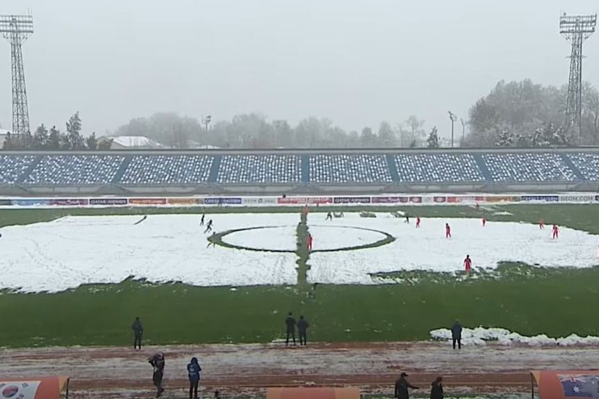 Two soccer teams play in an outdoor field half-covered with snow