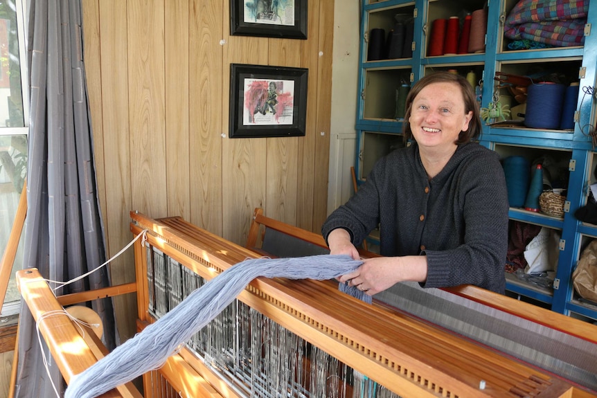 A woman standing in front of a loom with thread on it.