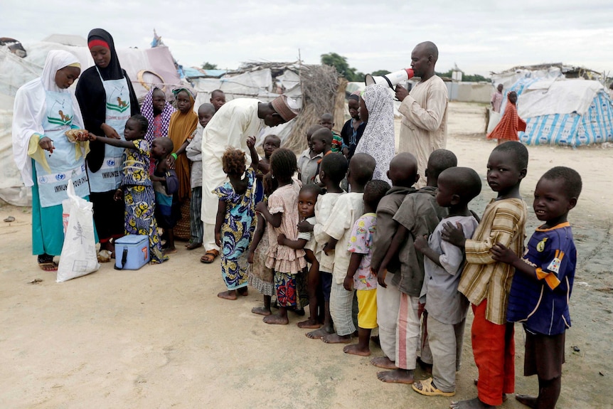 People line up amid tents as health officials administer polio vaccine to children at a camp.
