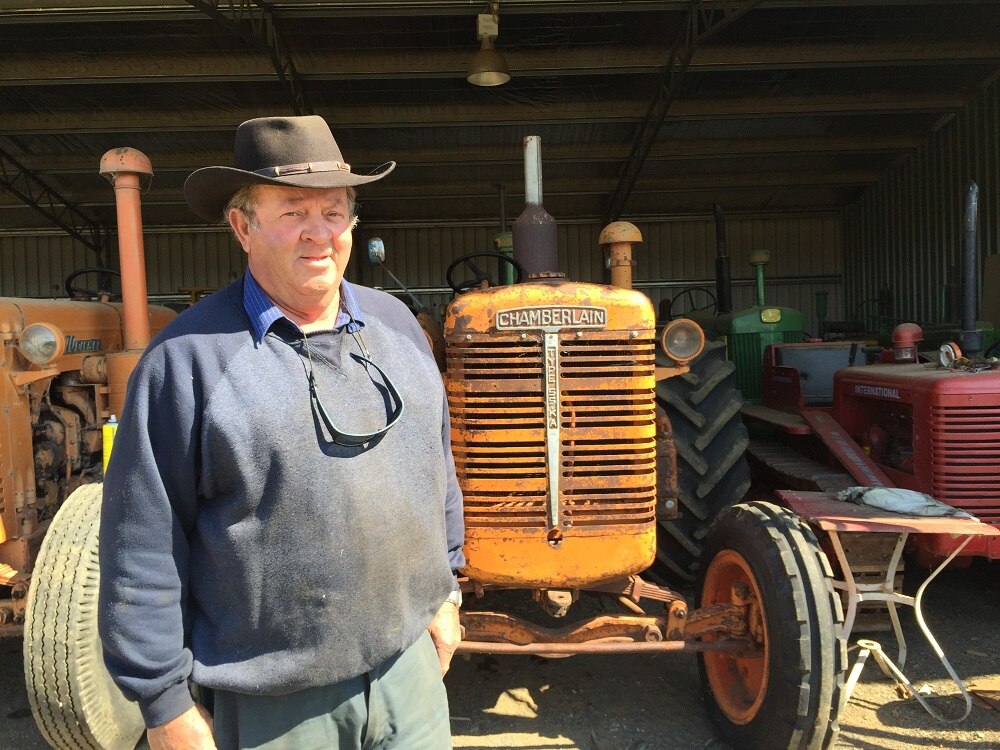 A farmer stands in front of an orange tractor