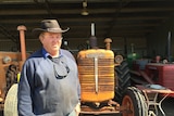 A farmer stands in front of an orange tractor