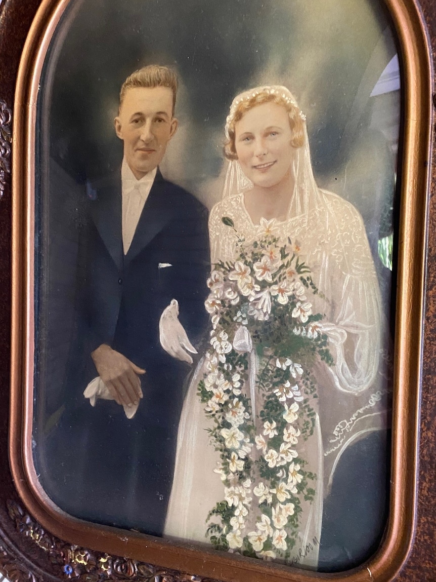A very old framed photo of a bride and groom and the bride's bouquet is a flowing arrangement of frangipani flowers