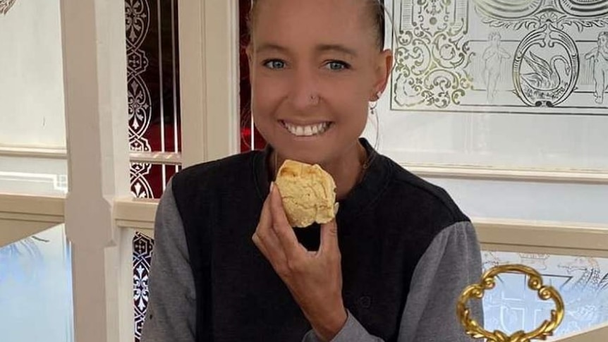 A young woman with a big smile, holding a scone at a high tea.